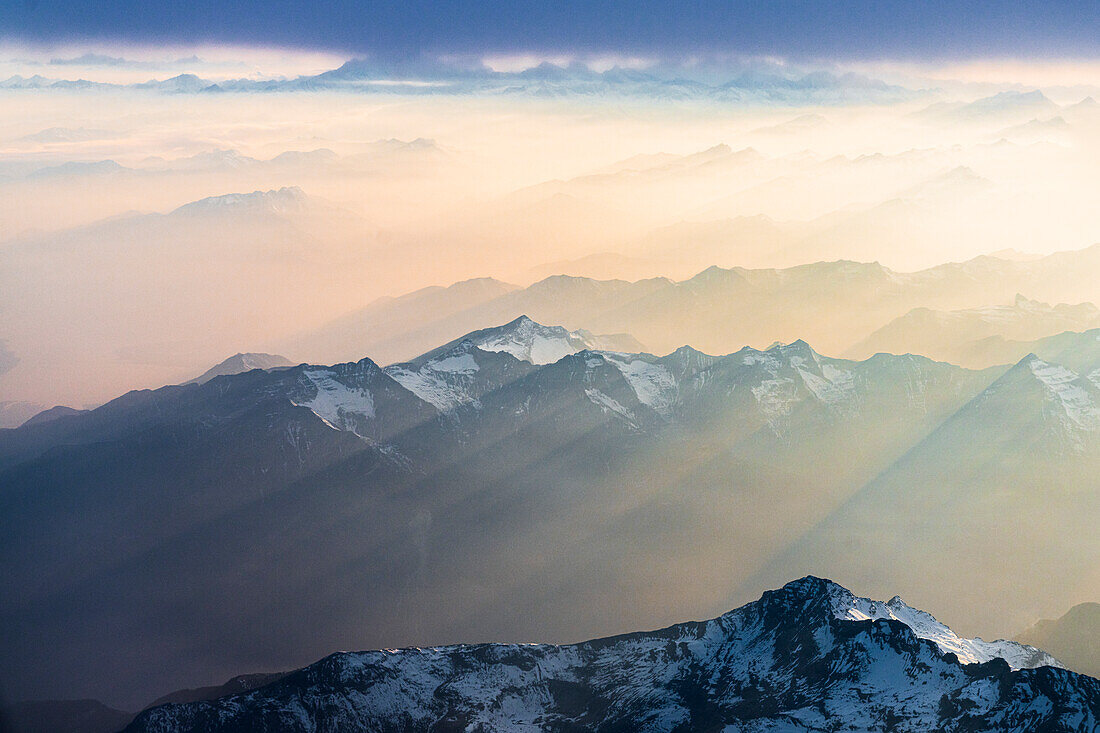 Flug über die schneebedeckten Gipfel der Lepontiner und Tessiner Alpen, beleuchtet von Sonnenstrahlen am romantischen Himmel bei Sonnenuntergang, Schweiz, Europa