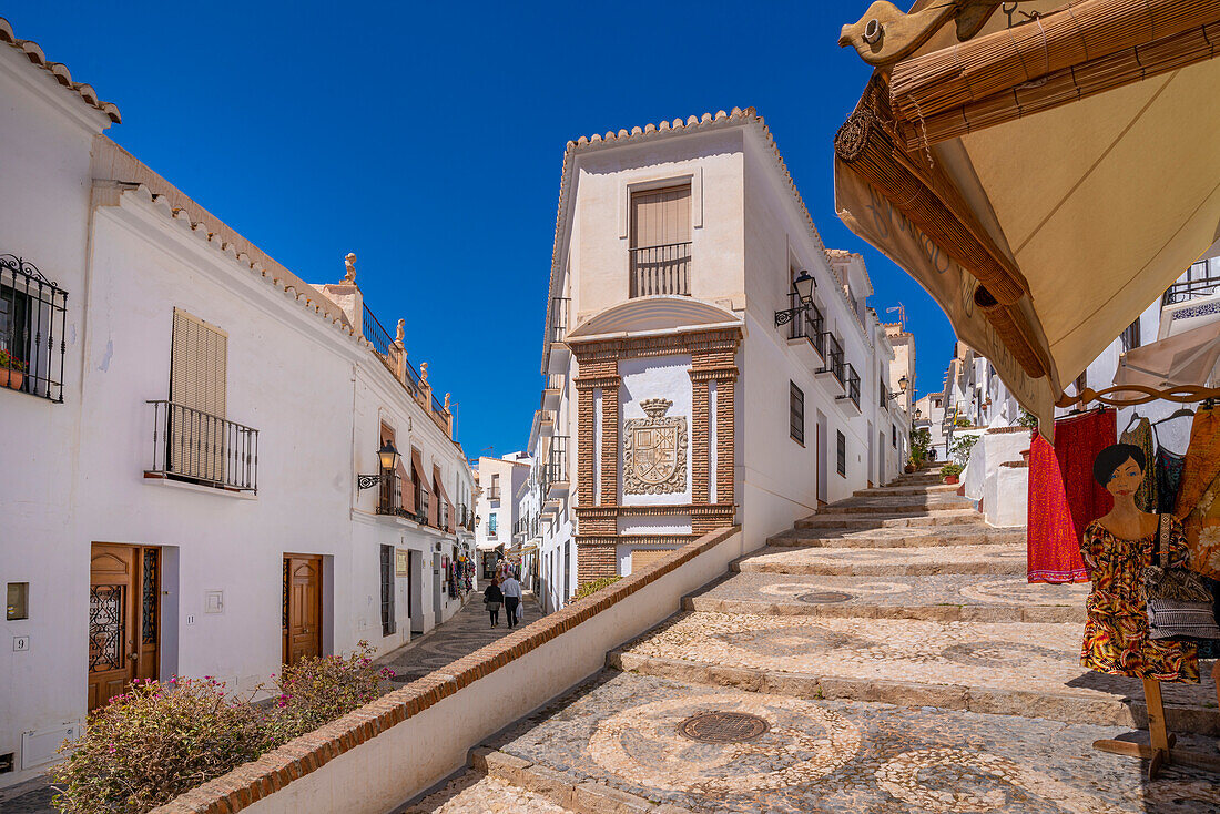 Blick auf weiß getünchte Häuser und Bekleidungsgeschäft in enger Straße, Frigiliana, Provinz Malaga, Andalusien, Spanien, Mittelmeer, Europa