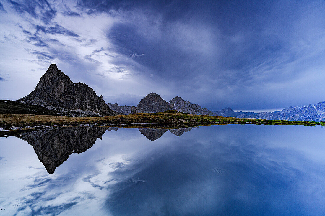 Ra Gusela und Tofane Gipfel spiegeln sich im Wasser unter dem bewölkten Himmel in der Abenddämmerung, Giau Pass, Dolomiten, Veneto, Italien, Europa