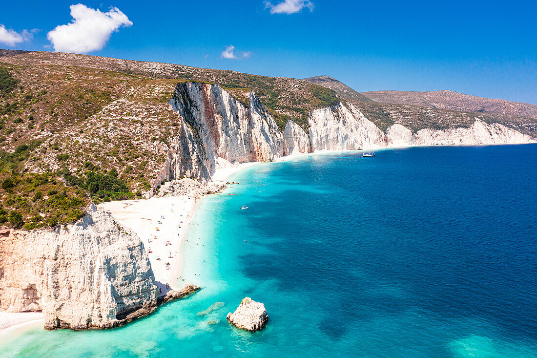 Tourists sunbathing at idyllic Fteri Beach set among cliffs and blue lagoon, overhead view, Kefalonia, Ionian Islands, Greek Islands, Greece, Europe