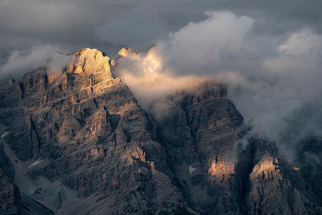 Sonnenuntergangslicht beleuchtet einige in Wolken und Nebel gehüllte Dolomitenfelsen, Dolomiten, Italien, Europa