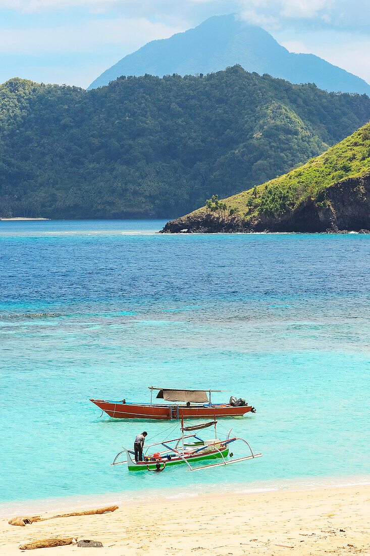 Strand der Insel Mahoro mit Ausflugsbooten und einem weit entfernten Vulkan auf Siau, Mahoro, Siau, Sangihe-Archipel, Nordsulawesi, Indonesien, Südostasien, Asien
