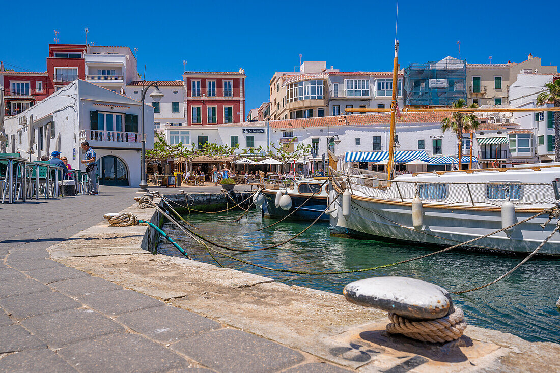 Blick auf bunte Cafés, Restaurants und Boote im Hafen vor blauem Himmel, Cales Fonts, Menorca, Balearen, Spanien, Mittelmeer, Europa