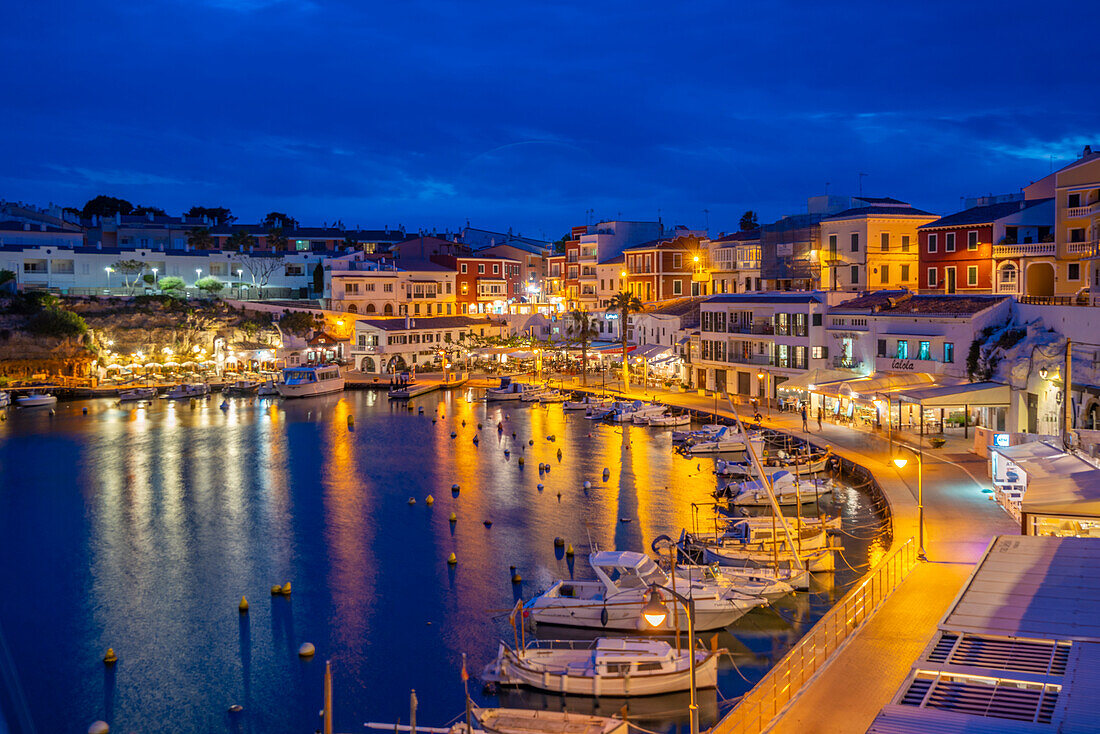 Blick auf Cafés, Restaurants und Boote im Hafen in der Abenddämmerung, Cales Fonts, Es Castell, Menorca, Balearische Inseln, Spanien, Mittelmeer, Europa