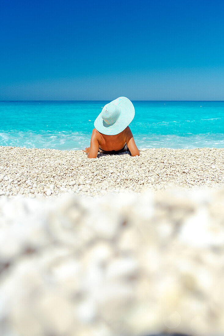 Frau mit Strohhut, die im Sommer am Strand liegt und das Meer betrachtet, Kefalonia, Ionische Inseln, Griechische Inseln, Griechenland, Europa