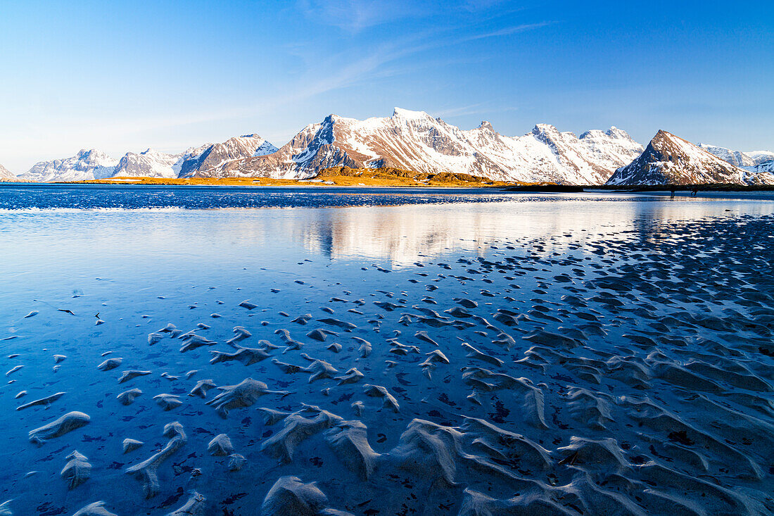 Wellen des kalten Meeres brechen an den Strand mit schneebedeckten Bergen im Hintergrund, Fredvang, Nordland, Lofoten, Norwegen, Europa
