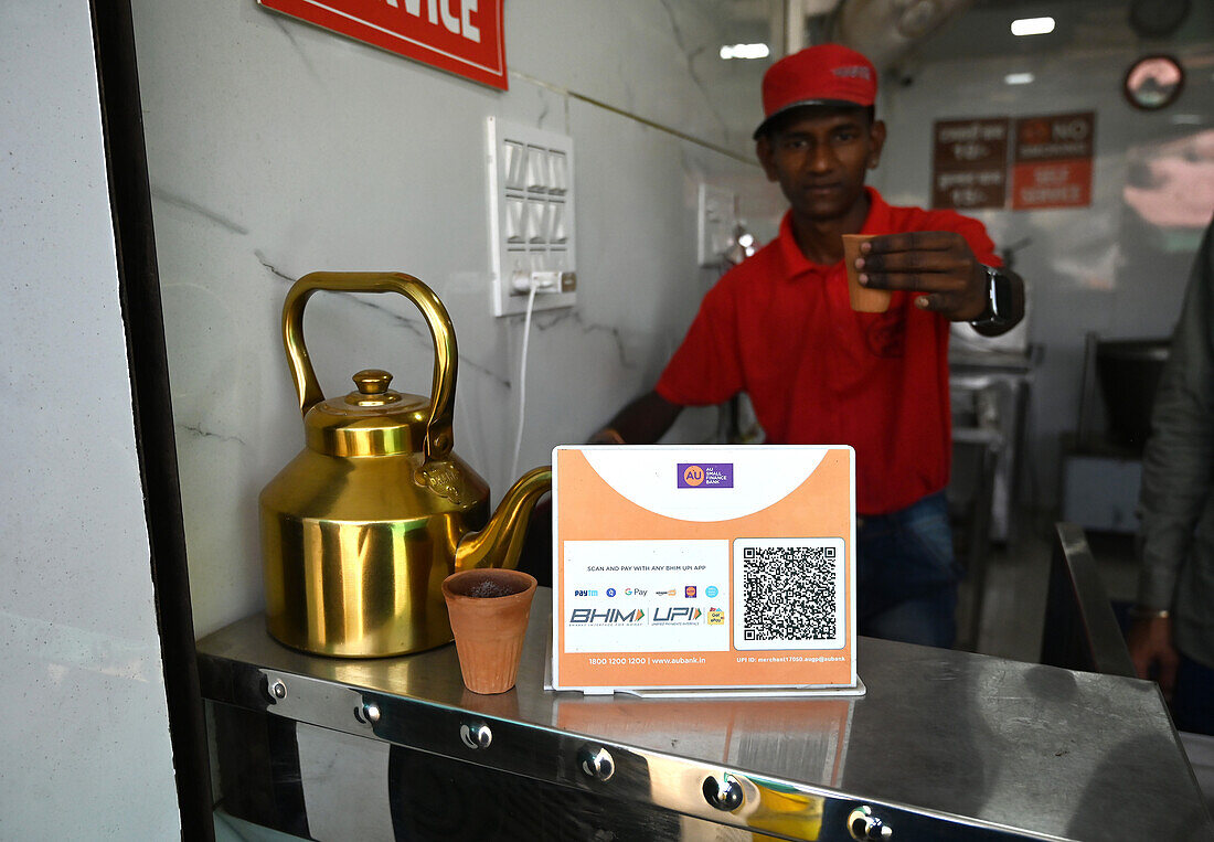 Chai wallah serving chai in old style terracotta disposable cups, with 21st century sign for payment by mobile phone, Mahisagar, Gujarat, India, Asia