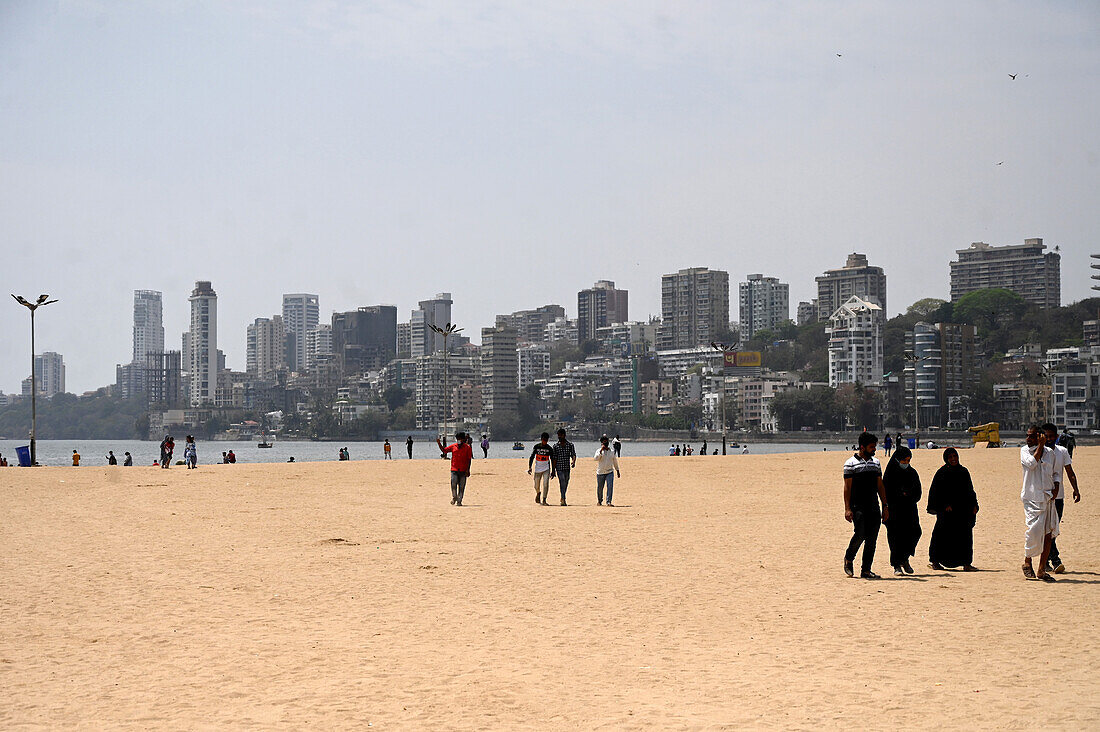 Menschen, darunter auch Muslime, die am Juhu-Strand spazieren gehen, im Hintergrund die Hochhäuser der Stadt, Mumbai, Indien, Asien