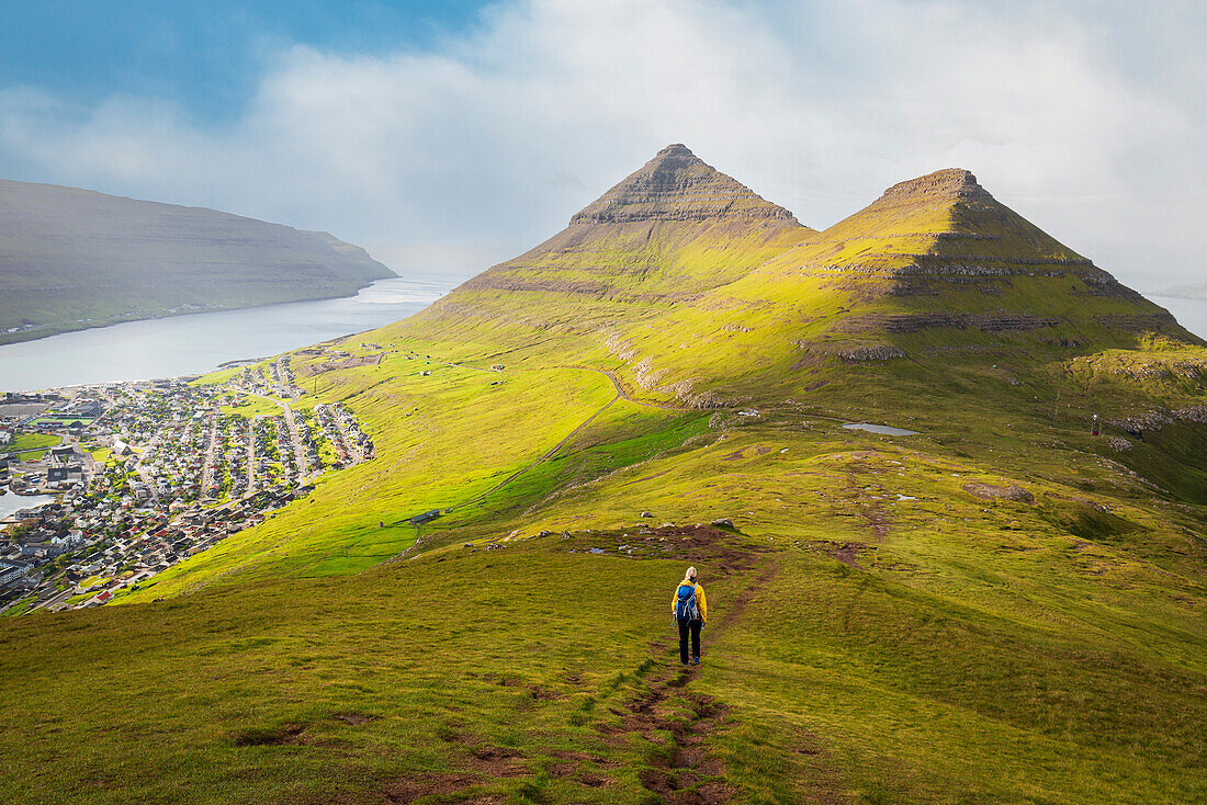 Hiker with yellow jacket walks down the mount Klakker, Klaksvik, Borooy island, Faroe Islands, Denmark, Europe
