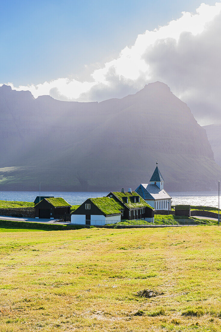 Blick auf die Kirche und die Grasdachhäuser im Dorf Vidareidi bei Sonnenuntergang, Insel Vidoy, Färöer, Dänemark, Europa