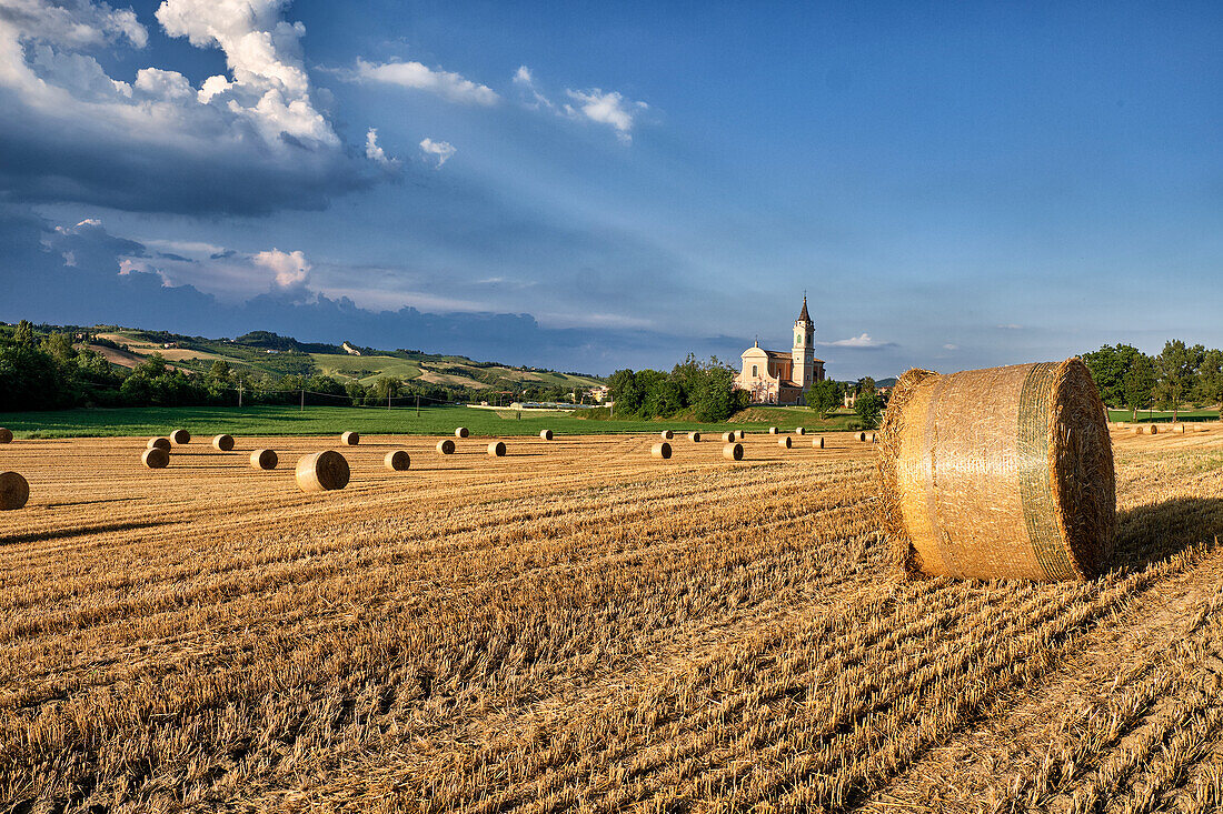 Italienische Landschaft mit einem Feld voller Heuballen und einer Kirche im Hintergrund, Emilia Romagna, Italien, Europa