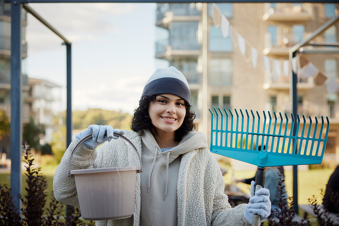 Portrait of smiling teenage girl holding rake and bucket