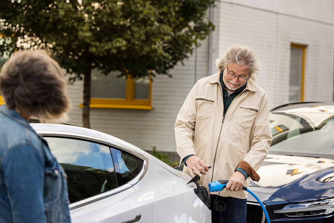 Senior man charging electric car outdoors