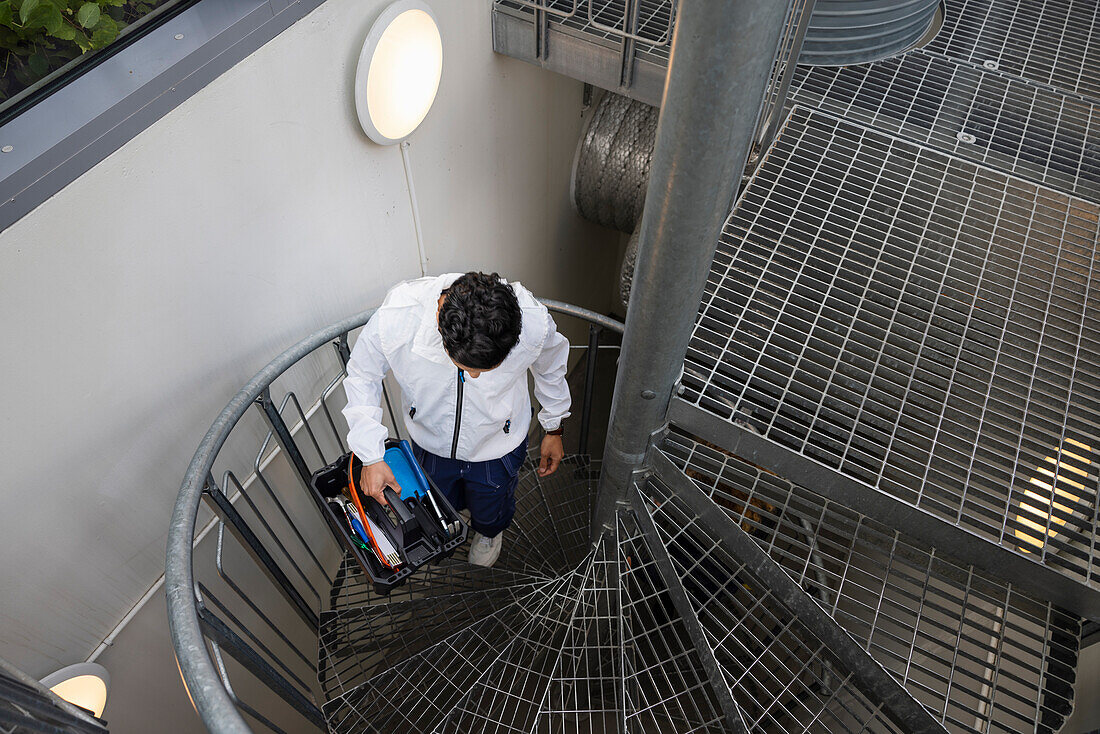 Junger männlicher Techniker trägt Werkzeugkasten auf Treppe