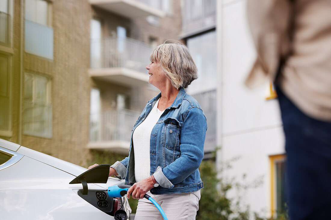 Senior woman charging electric car