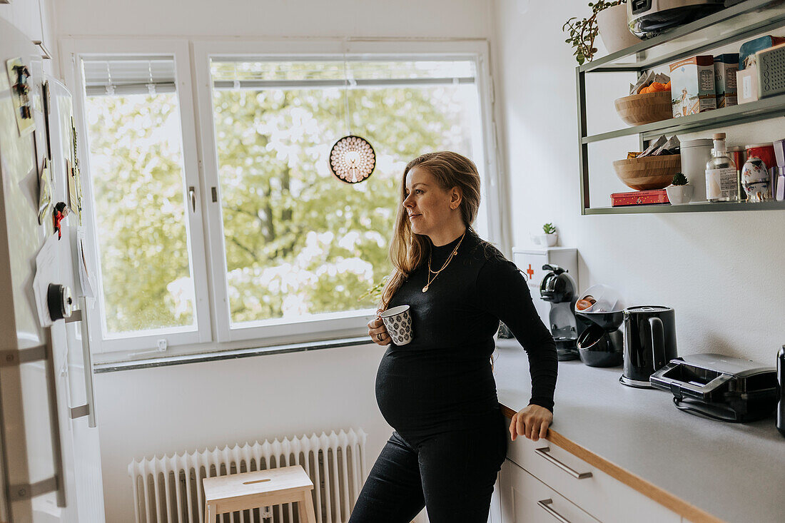 Pregnant woman holding cup in kitchen