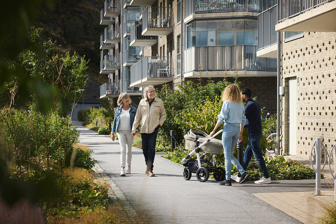 Senior and young couple with baby stroller walking in residential area