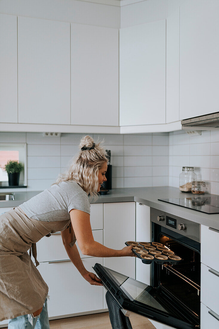 Frau in der Küche schiebt Muffins in den Ofen