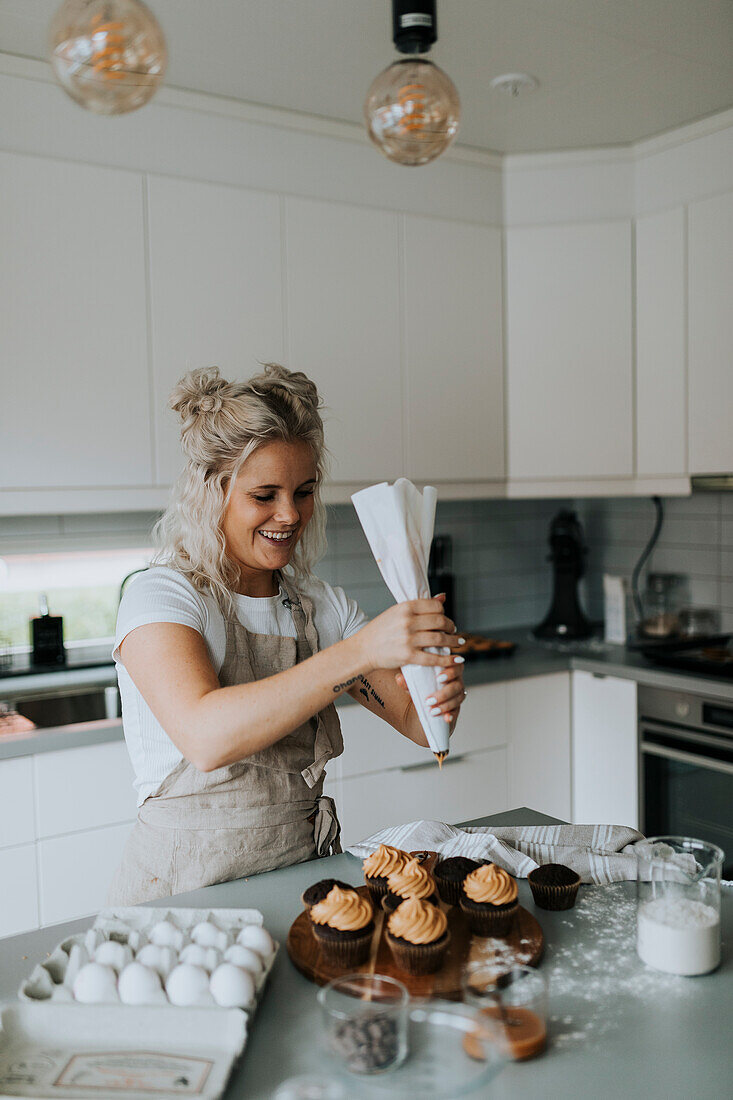 Frau streicht Zuckerguss auf Muffins