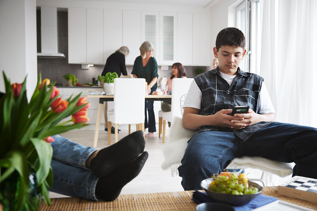 Teenage boy sitting in living room and using phone