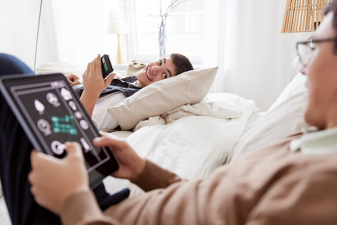 Brüder liegen auf dem Bett und benutzen Telefon und Tablet