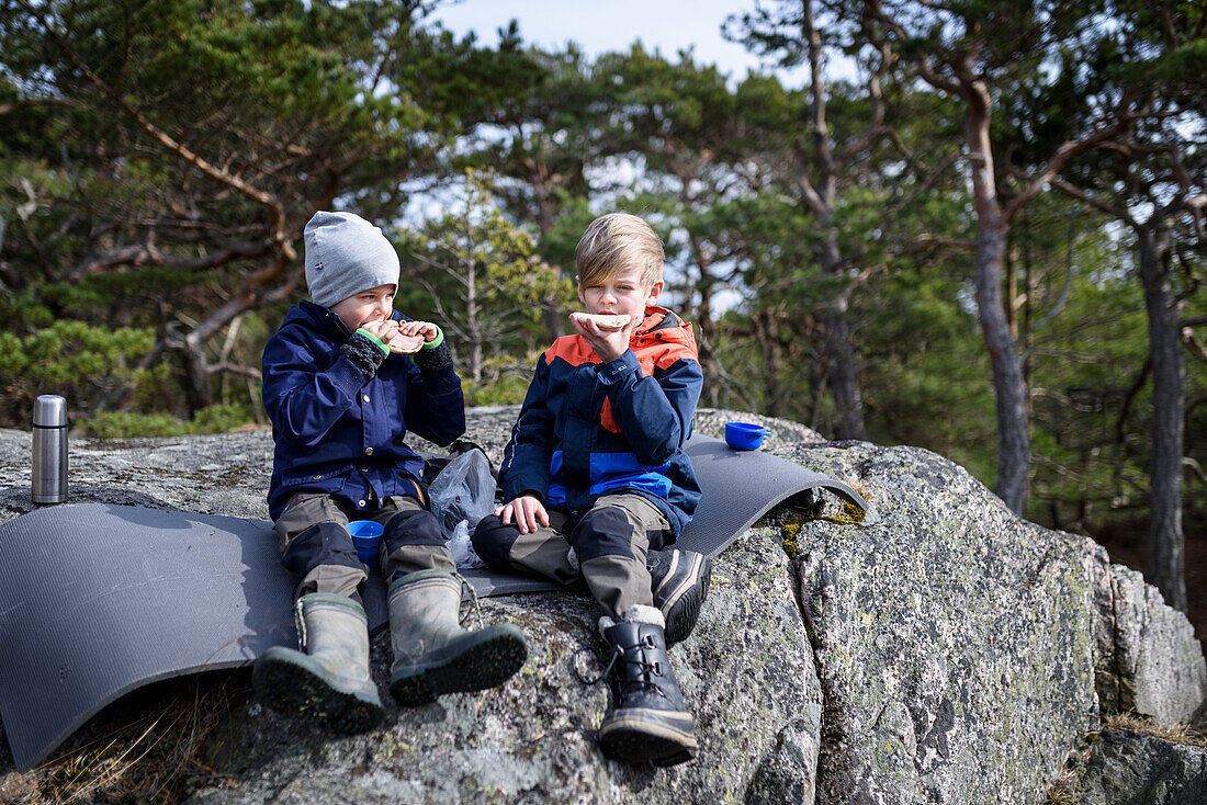 Jungen sitzen auf einem Felsen und essen