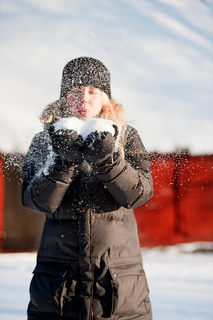 Young woman with handful of snow and blowing into it