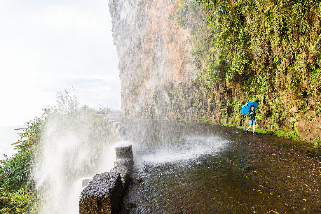 Junge mit Regenschirm unter Wasserfall