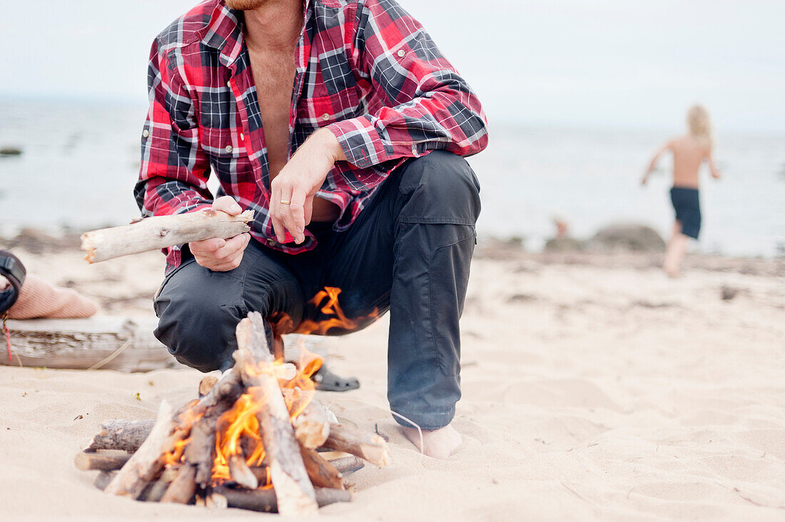 Man crouching next to campfire on beach