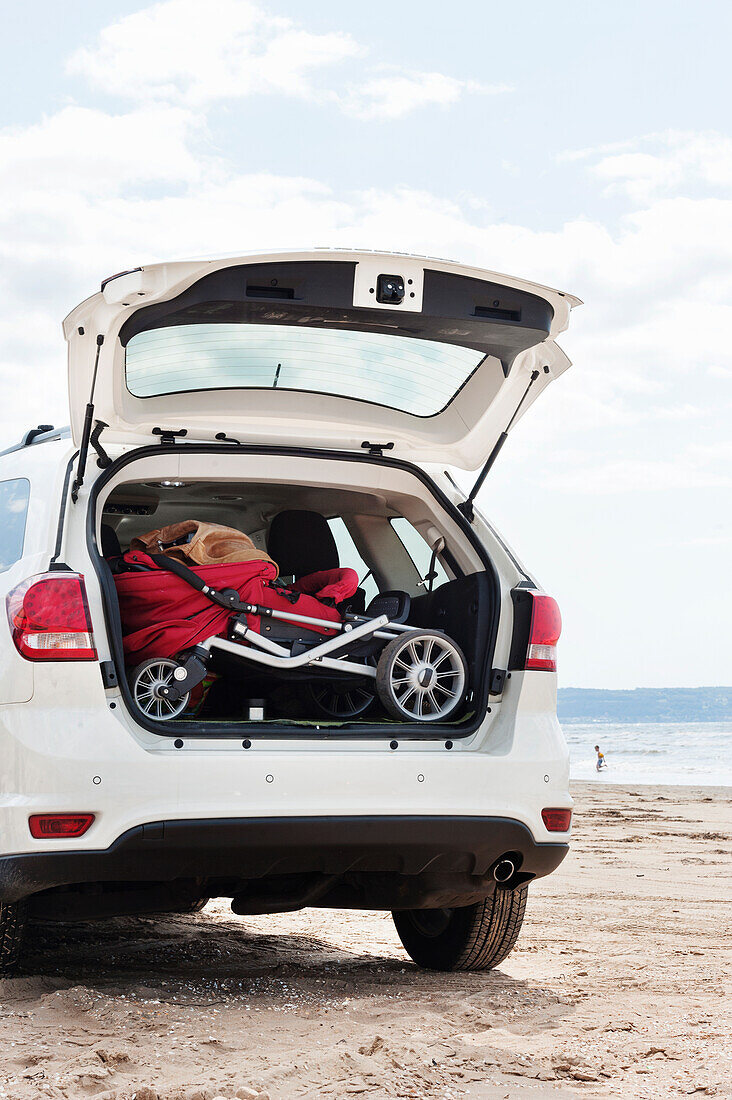 Baby carriage in car trunk on beach by sea