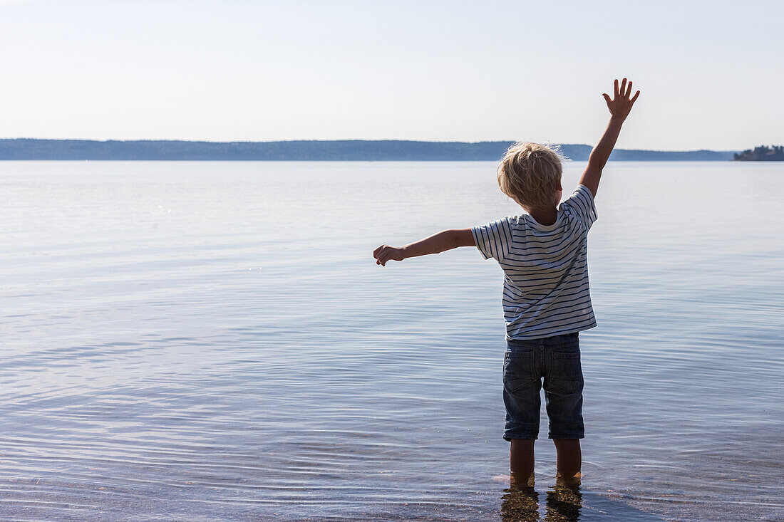 Junge im Meer stehend mit erhobenen Armen