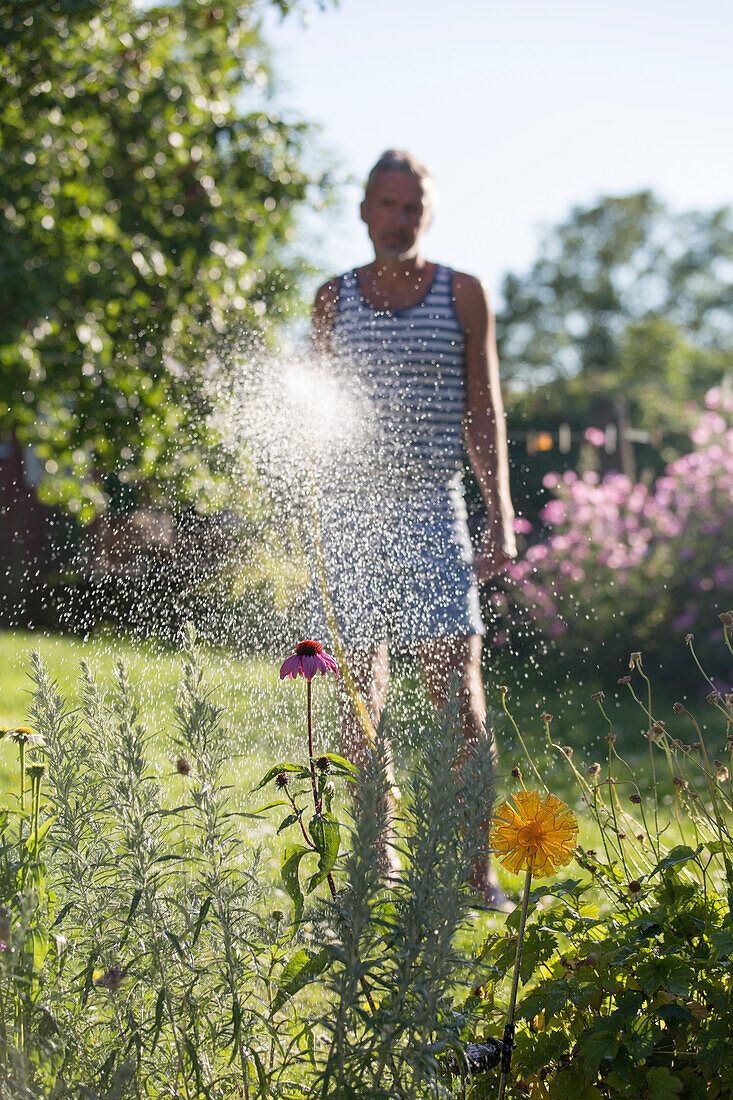 Mann gießt Blumen im Garten