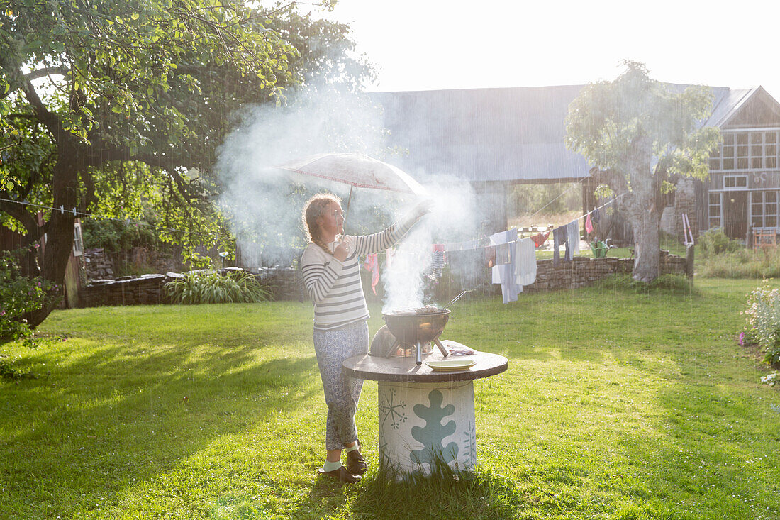 Girl with umbrella having barbecue in garden