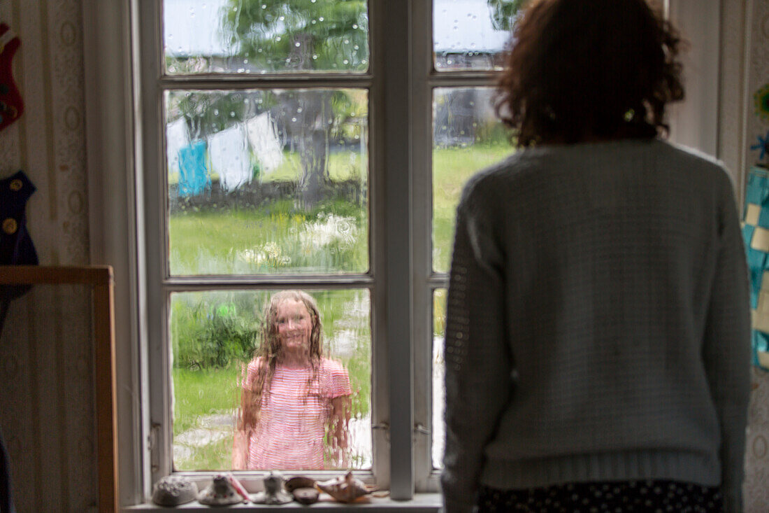 Mother and daughter looking through window at each other