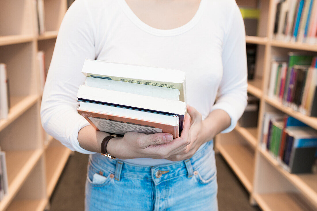 Frau hält Bücher in einer Bibliothek