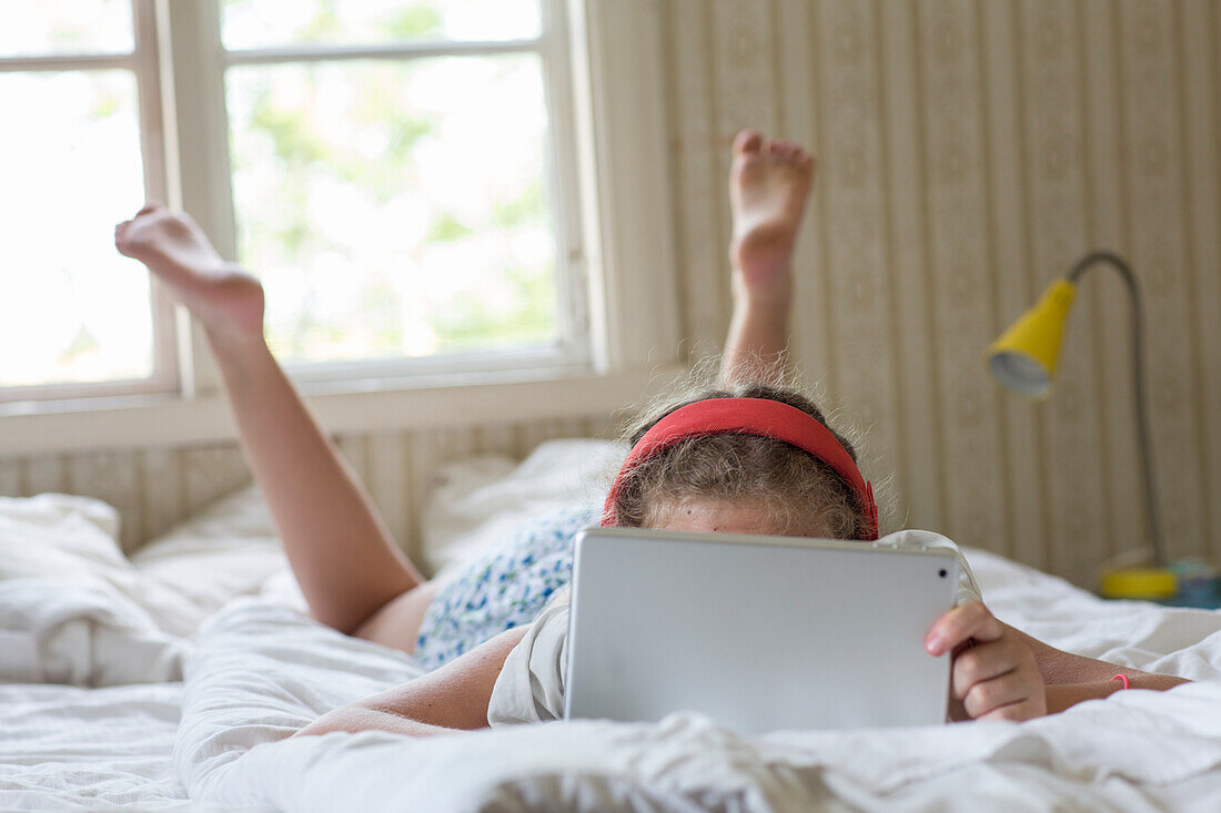 Mädchen liegt auf dem Bett und benutzt ein Tablet