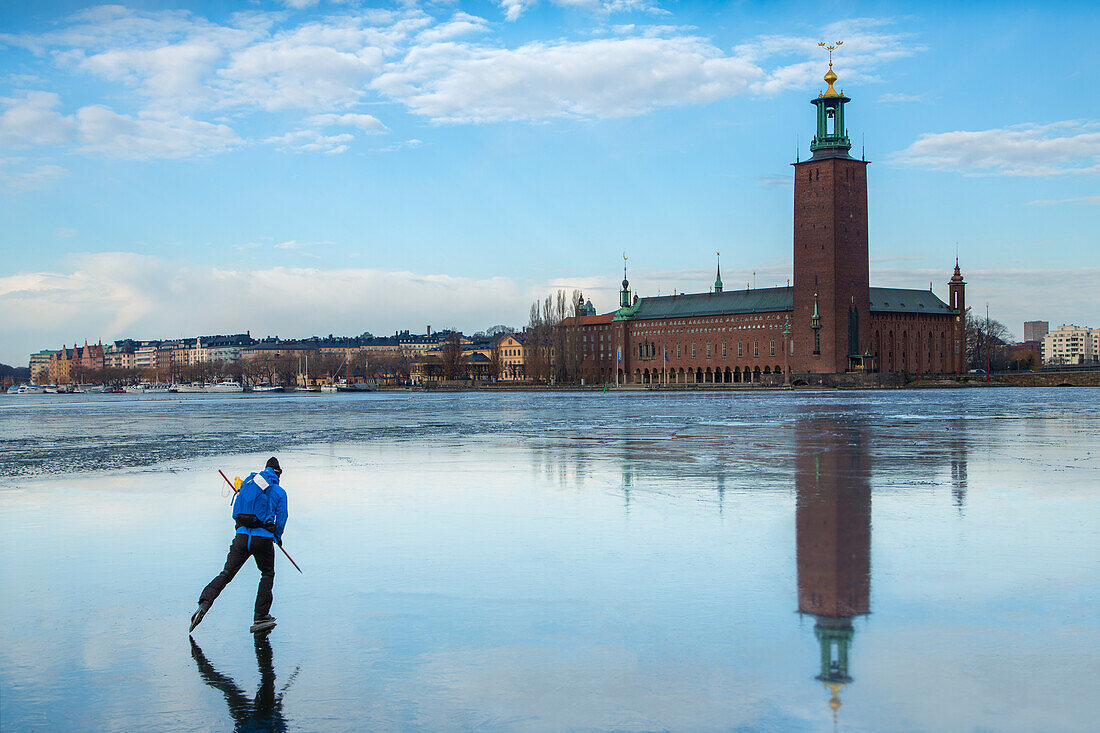 Person beim Schlittschuhlaufen auf dem Meer, im Hintergrund das Rathaus von Stockholm, Schweden