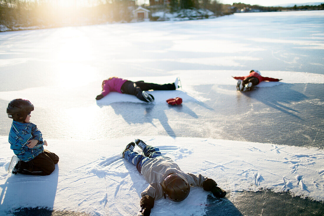 Mother with children making snow angels on frozen lake