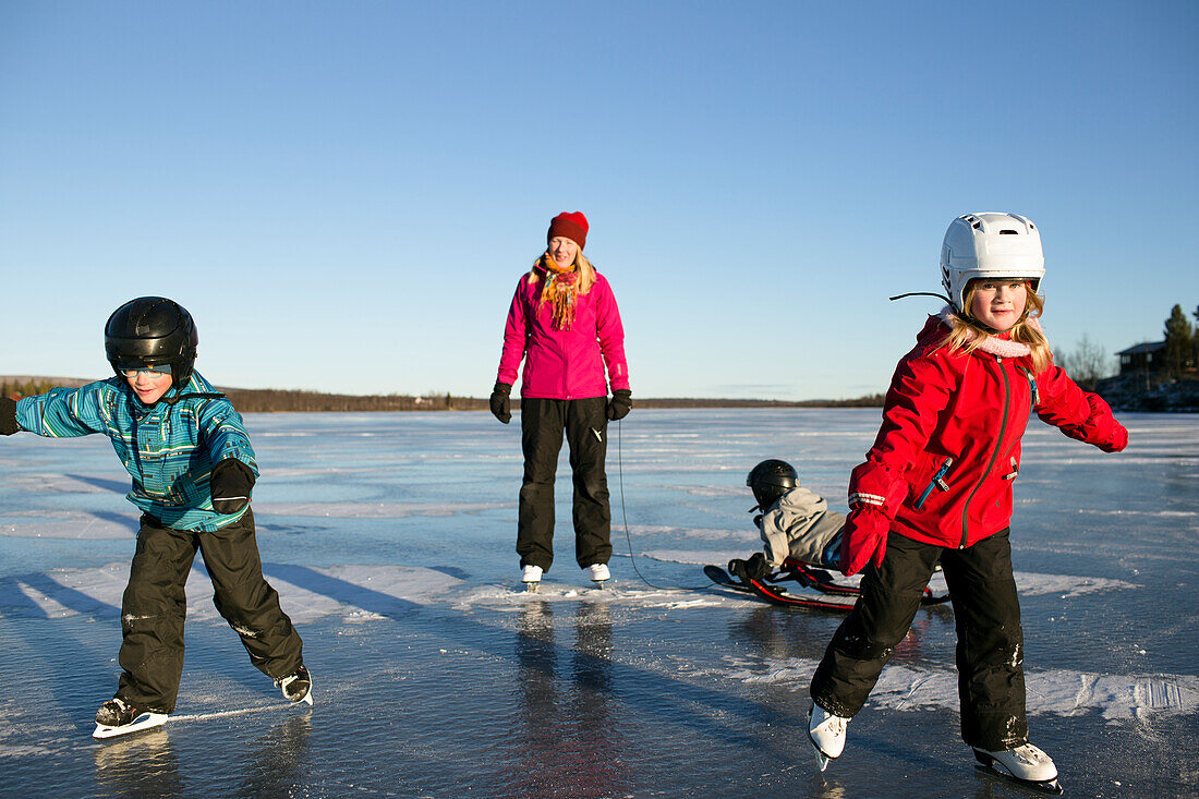 Mutter mit Kindern beim Schlittschuhlaufen am See