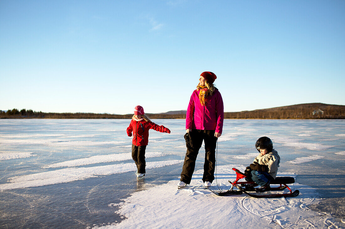 Mutter mit Kindern beim Schlittschuhlaufen am See