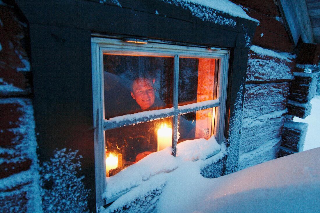 Man looking through window of log cabin