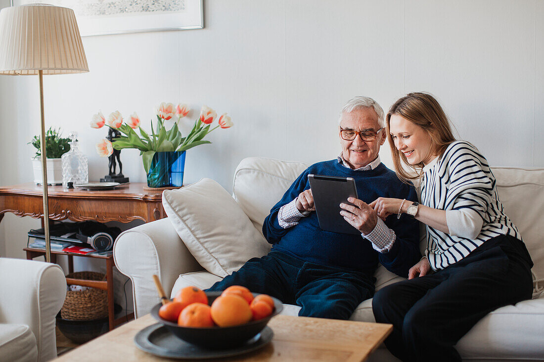 Senior man with adult granddaughter using digital tablet