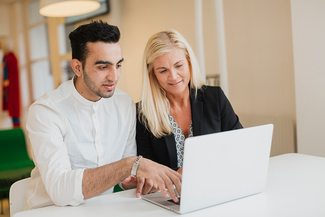 Man and woman using laptop together in office