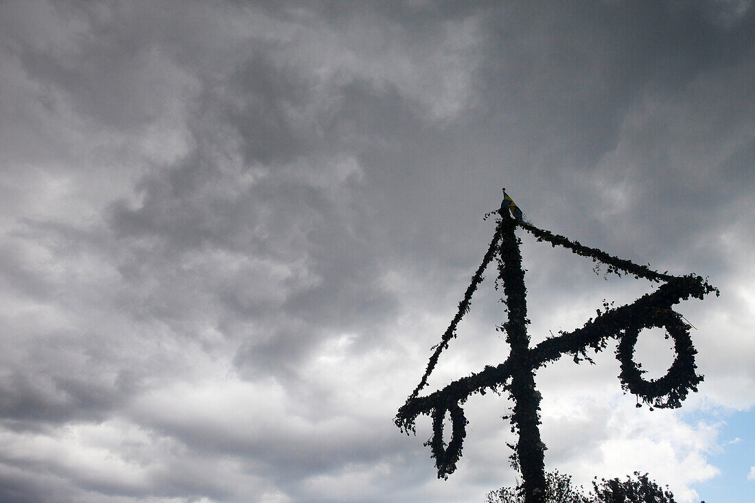 Silhouette eines Maibaums vor Gewitterwolken