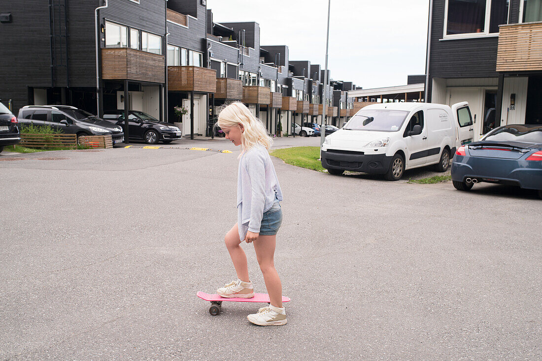 Blond girl with pink skateboard on street