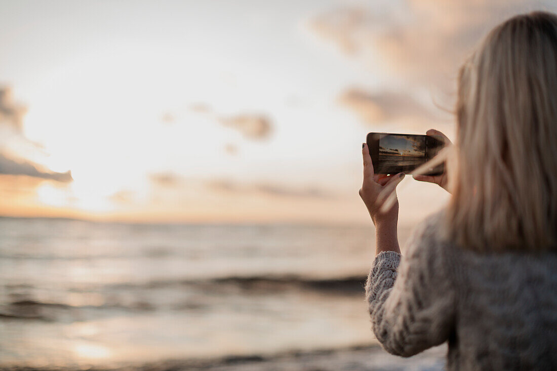 Woman photographing sunset with smartphone
