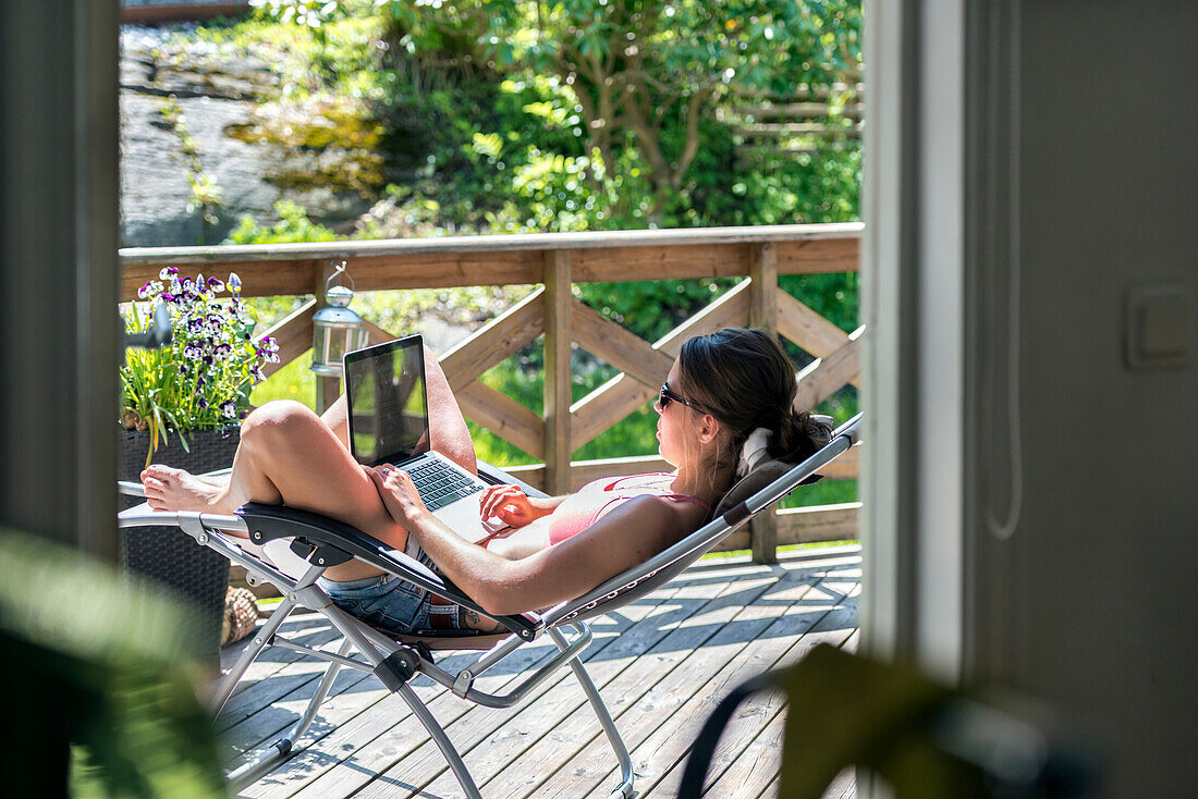 Junge Frau mit Laptop auf der Sonnenliege