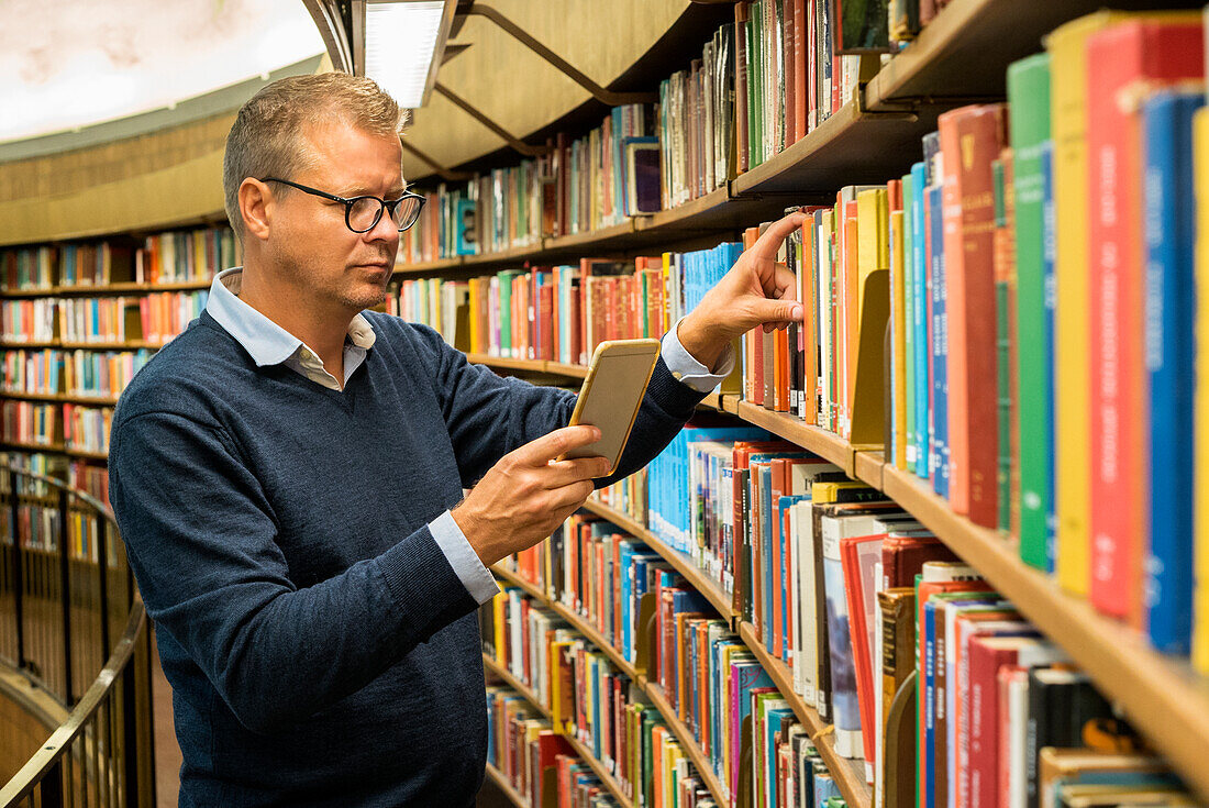 Mann wählt ein Buch in der Bibliothek aus