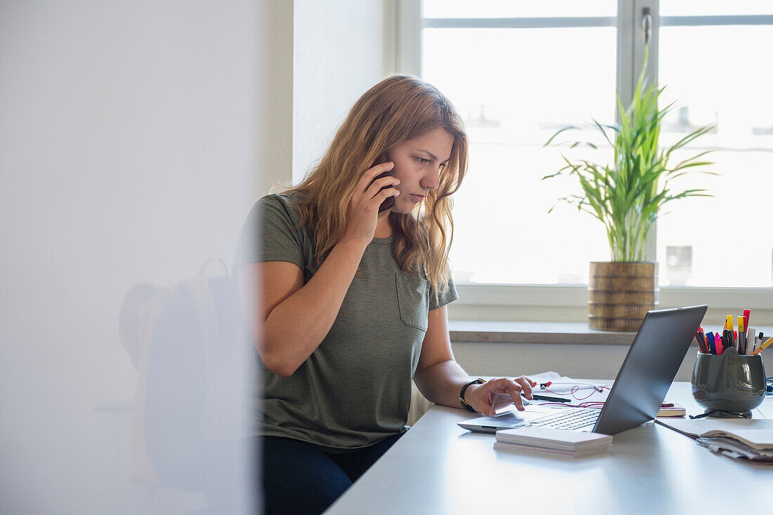 Woman working on laptop and using phone in office