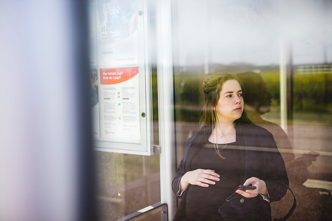 Schwangere Frau sitzt am Busbahnhof